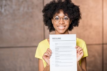 Photo of an woman in a yellow shirt holding a piece of paper with the text Resume at the top
